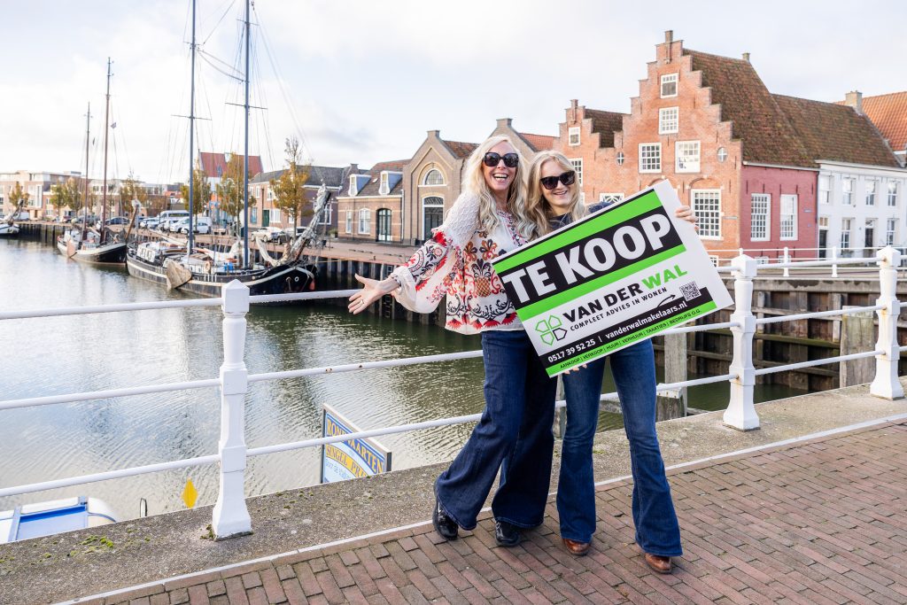 Janneke van der Wal samen met collega Ilse bij een te koop-bord van Van der Wal Makelaars.