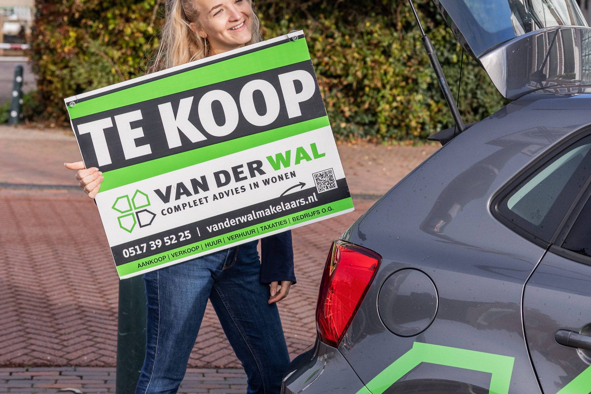 Ilse, assistent makelaar bij Van der Wal Makelaars, brengt een te koop-bord.